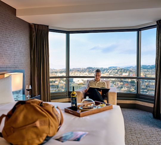 A man is reading and dining in a guest room with city view