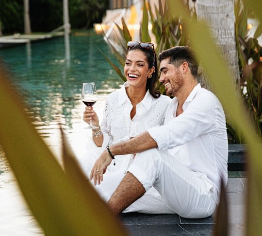 Couple sitting at edge of pool with wine glass
