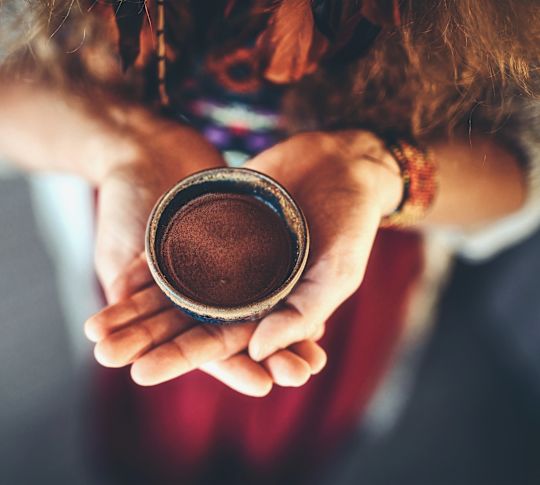 Woman's hands holding small pot of cacao powder