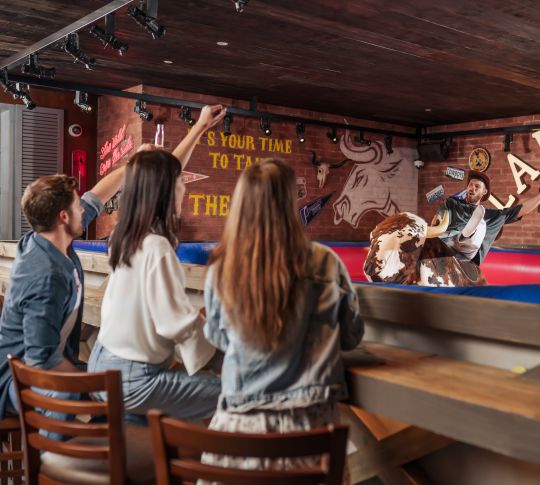 Man riding on bucking bronco while friends cheer