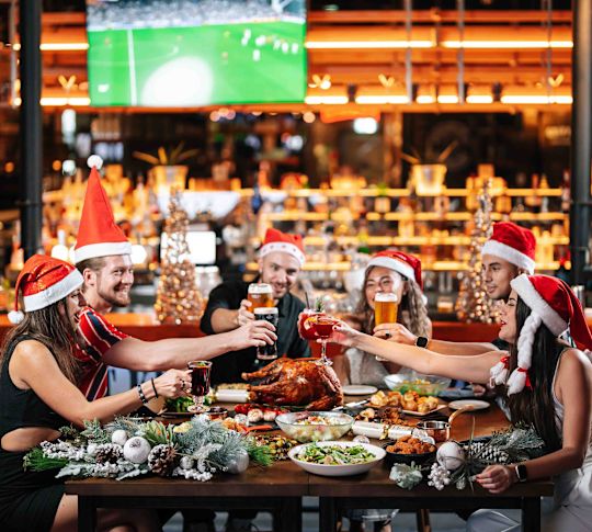 McGettigan's Factory people in Santa hats at table cheering with beers and bar behind them