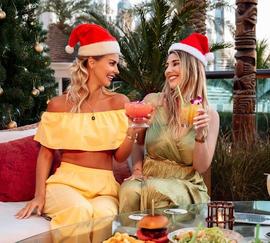 Tahitian Village outdoor terrace with two women holding cocktails in Santa hats