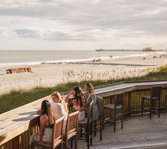 Women sitting at beach bar looking out on to beach and sea