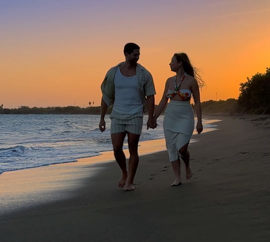 زوجان يحملان أيديهما أثناء السير على الشاطئ في وقت غروب الشمس