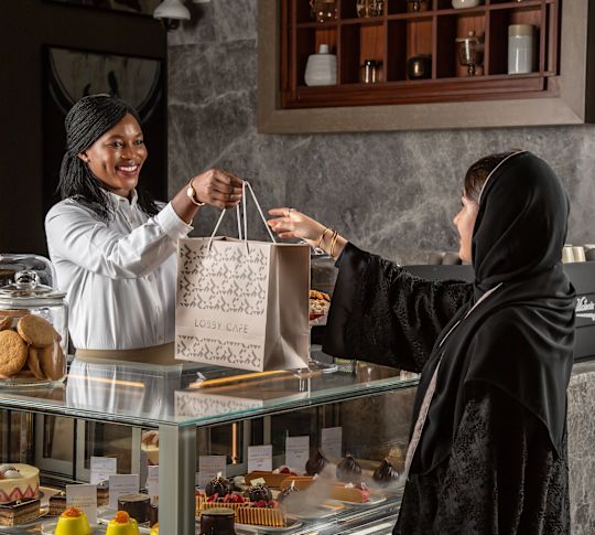 Das Teammitglied des Lobby Cafes übergibt dem Gast eine Essenstasche