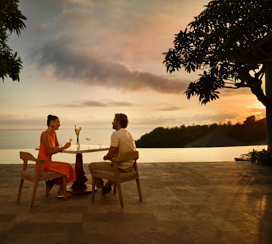 Coppia che sorseggia un drink all'aperto in una villa con vista sull'acqua al tramonto