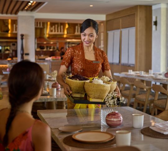 Un membre du personnel s'approche d'une table avec plateau et sourit au client