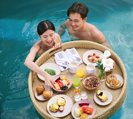 Coppia che fa colazione con un cesto galleggiante in piscina