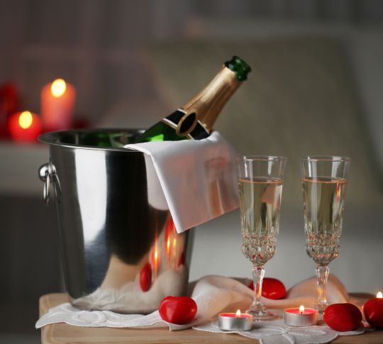 Champagne glasses and rose petals for celebrating Valentines Day, on dark background