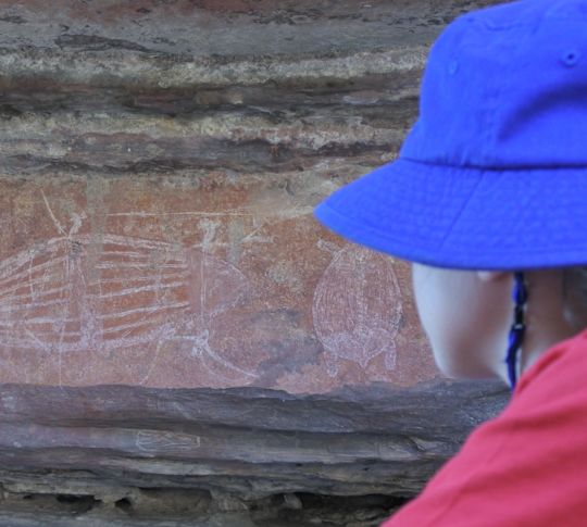 La persona con il cappello guarda i petroglifi della grotta