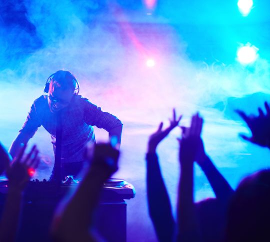 Energetic deejay standing in front of dancing people in club