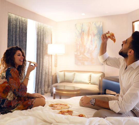 A smiling couple sharing room service pizzas