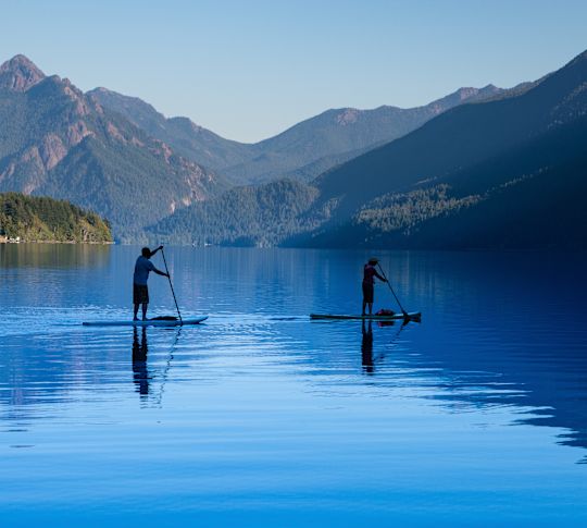 People Paddle Boarding in a River with Mountains in Background