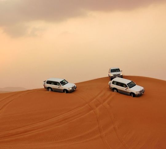 Desert scene with multiple white 4x4 vehicles driving on the sand dunes.