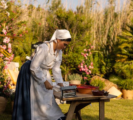 A Woman Wearing a Traditional Attire in a Garden, Is Setting a Machine on a Table to Make Pies-transition