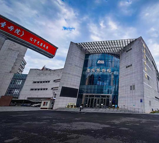 Modern Shenyang Palace Museum cu intrare curbată din sticlă, exterior din piatră albă și clădiri învecinate înalte.
