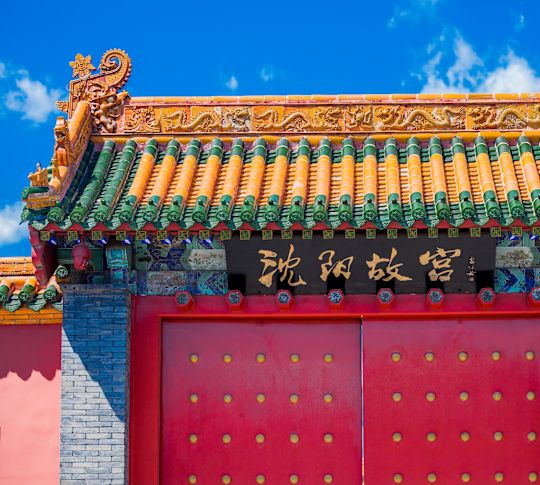 Poartă tradițională a palatului chinezesc cu uși cu ștuț roșu, detalii ale acoperișului sculptat și o placă cu litere aurii cu Palatul Imperial Shenyang.