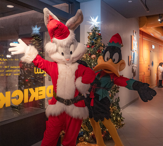 bugs bunny and daffy duck, with holiday outfits, standing in the lobby by the gift shop