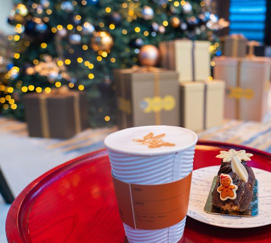 a plate with holiday cake and a cappuccino, holiday tree and gifts
