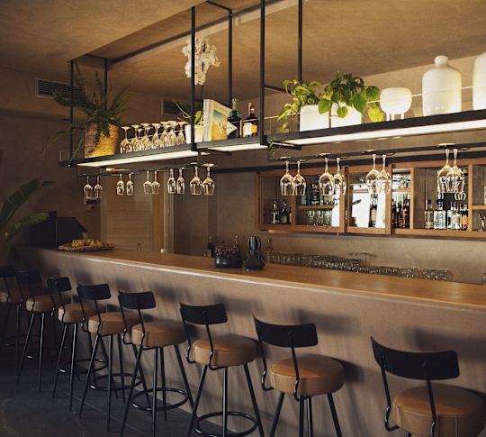 Yüksek ahşap tabureler, asılan şarap bardakları, saksılı bitkiler ve şişeler gösteren ahşap raflar bulunan mavi bar.