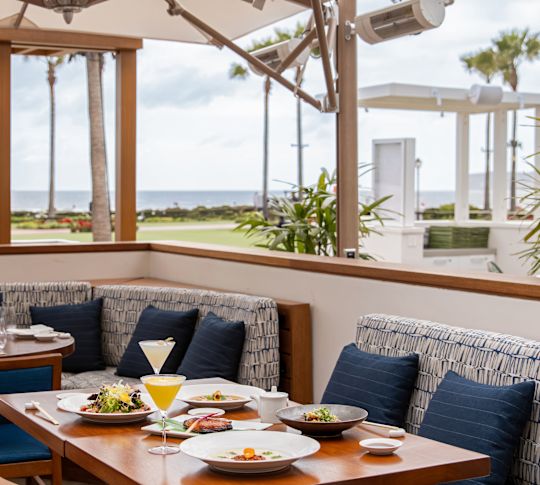Table de salle à manger dans le patio du restaurant Nobu del Coronado avec entrées et boissons, vue sur l'eau