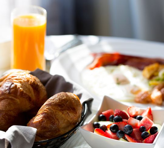 Gros plan sur un bol de baies, un panier de pâtisseries et un verre de jus d'orange