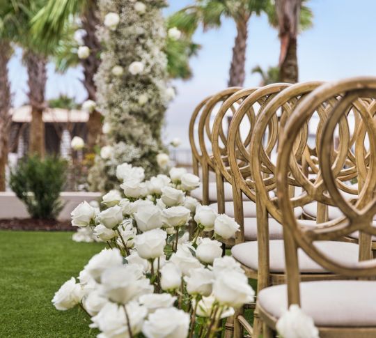 Detail of stunning outdoor on-site wedding ceremony with aisles of chairs and white roses.