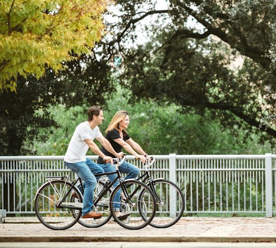 A man and a woman cycling through the park in late summer