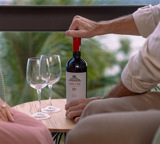 Man opening a bottle of wine that's on table with 2 wine glasses
