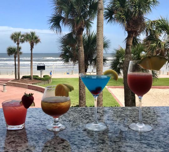 Selection of different cocktails on outside bar with palm trees and ocean in background