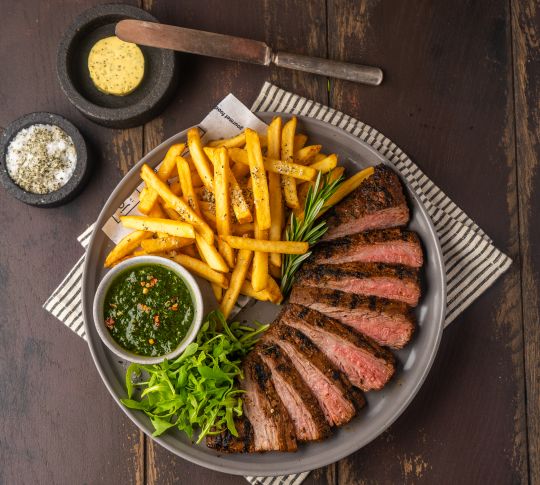 Steak and fries with sides of sauce, herb butter, and seasoning