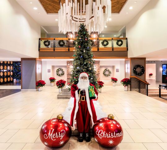santa figurine standing in front of christmas tree in hotel lobby