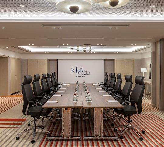 Meeting room with a long conference table, black chairs, and a projection screen