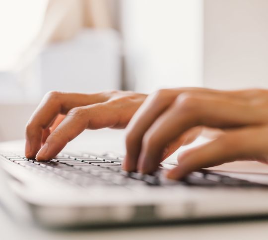 Gros plan de mains tapant sur un clavier d'ordinateur portable