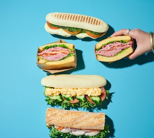 En kvinnas hand som håller en Ham Sandwich, på ett bord med ett urval av smörgåsar