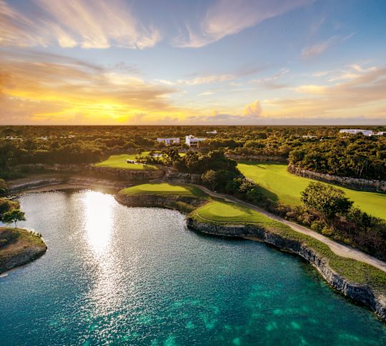 Luftaufnahme eines Golfplatzes mit Bäumen und einer Wasseranlage bei Sonnenuntergang