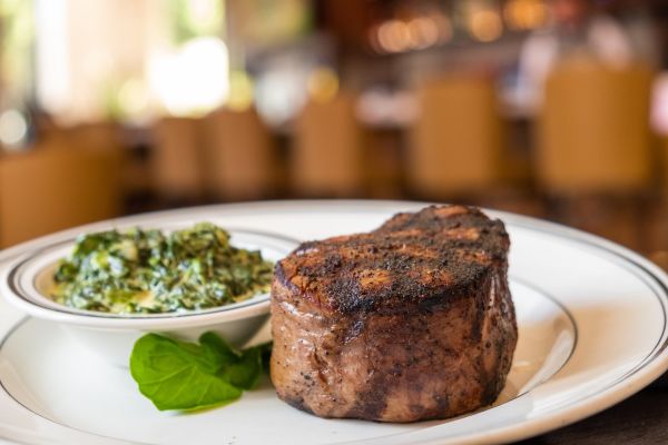 Filet Steak on a plate with a bowl of greens