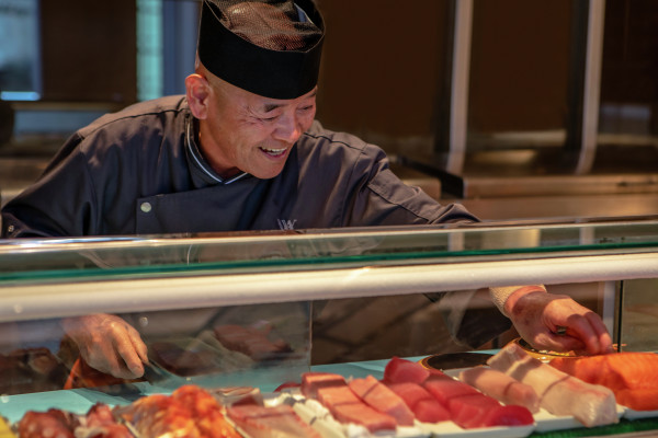 Chef Making Sushi Rolls with a Variety of Fish in Clear Covered Bar