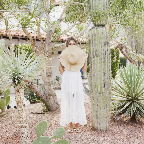 Woman holding hat in front of face, standing by cactus