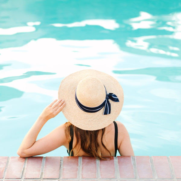 Woman in pool, with hand on hat