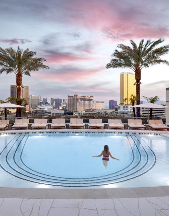 Woman standing in pool with palm trees framing skyline viewarby