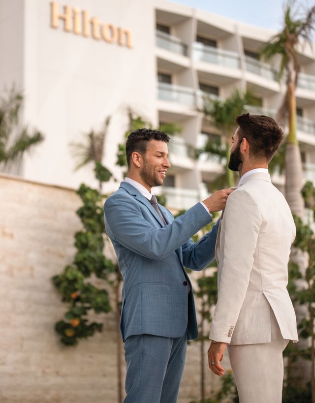 One man fixes another mans tie in front of a Hilton hotel