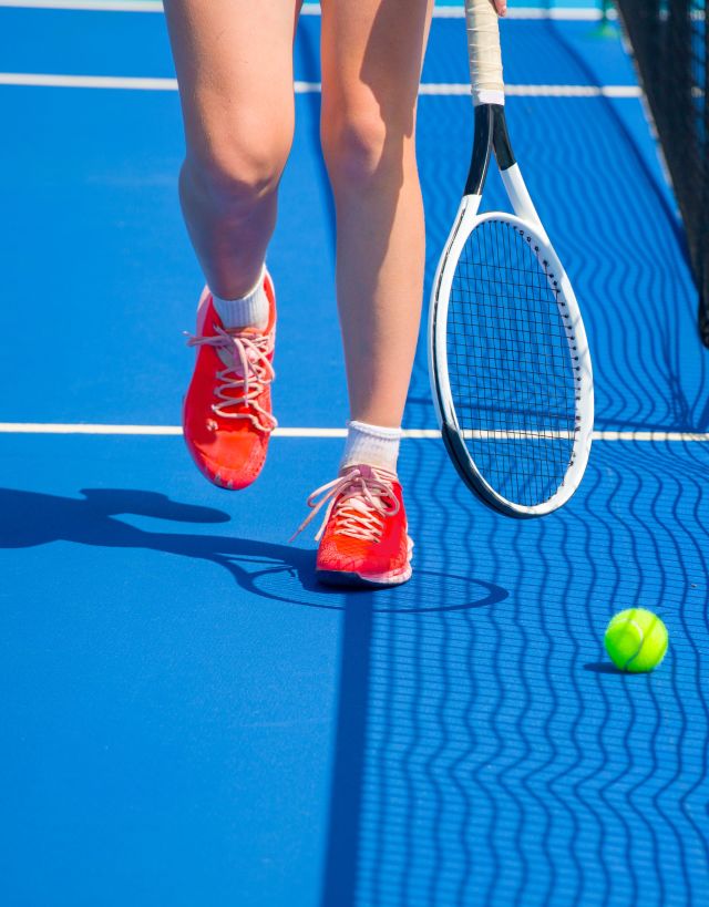 Woman's legs on tennis court with racket and ball