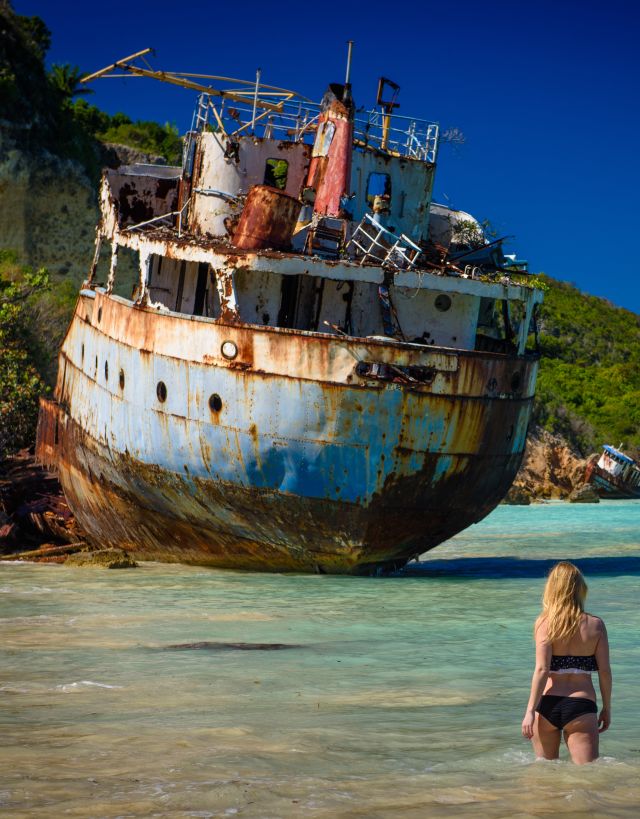 Woman wading in ocean with shipwreck in front of her