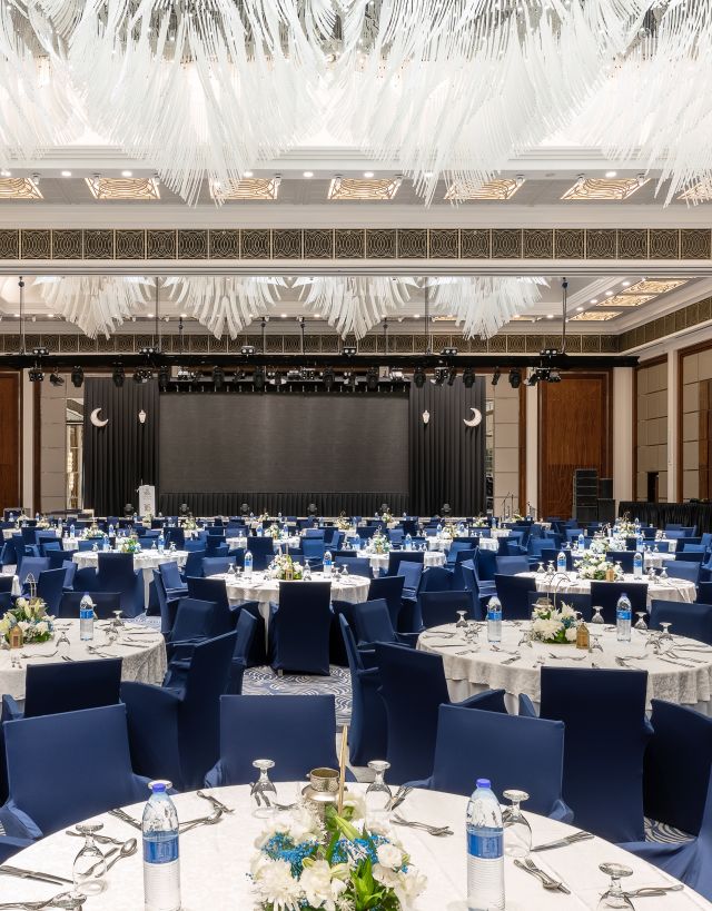 Al Joud Ballroom setup with white covered round tables and blue covered seats