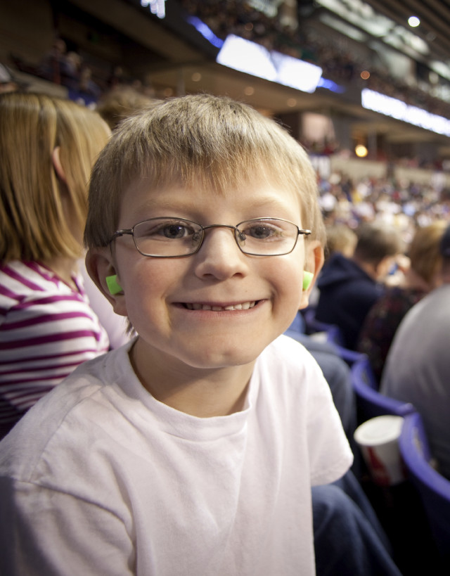 Young Boy Wearing Eyeglasses and  Green Earplugs at Sporting Event