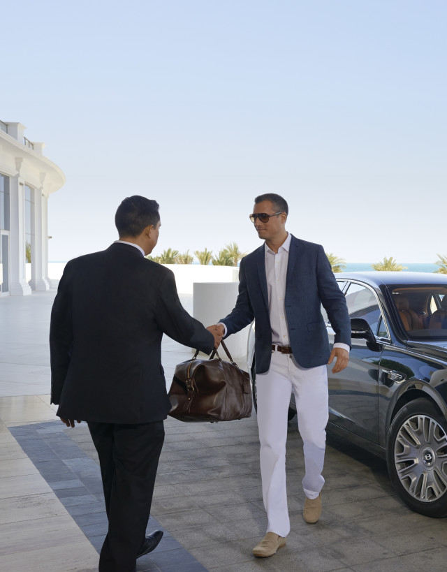 Man handing bag to valet at entrance to hotel after exiting luxury car