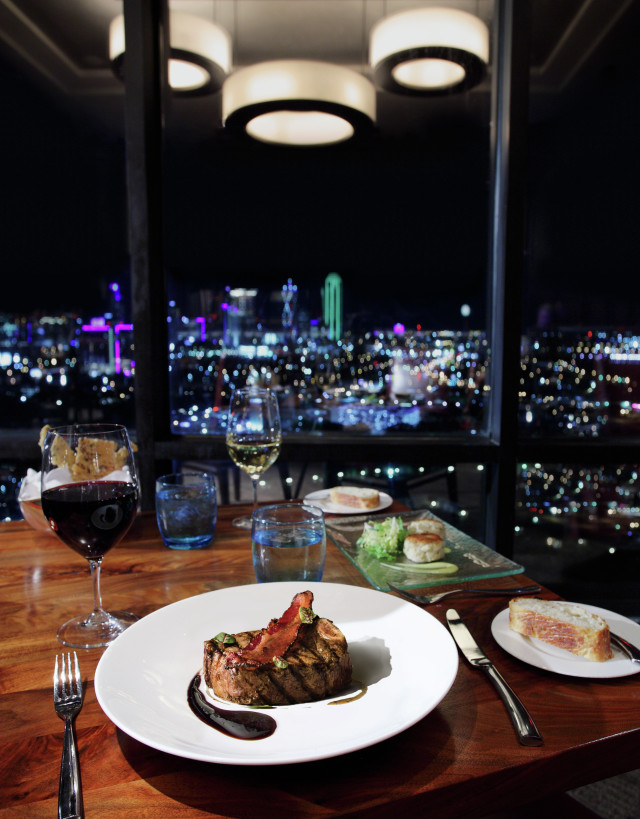 Steak on plate with Dallas at night in background