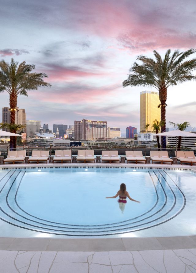 Woman standing in pool with palm trees framing skyline viewarby