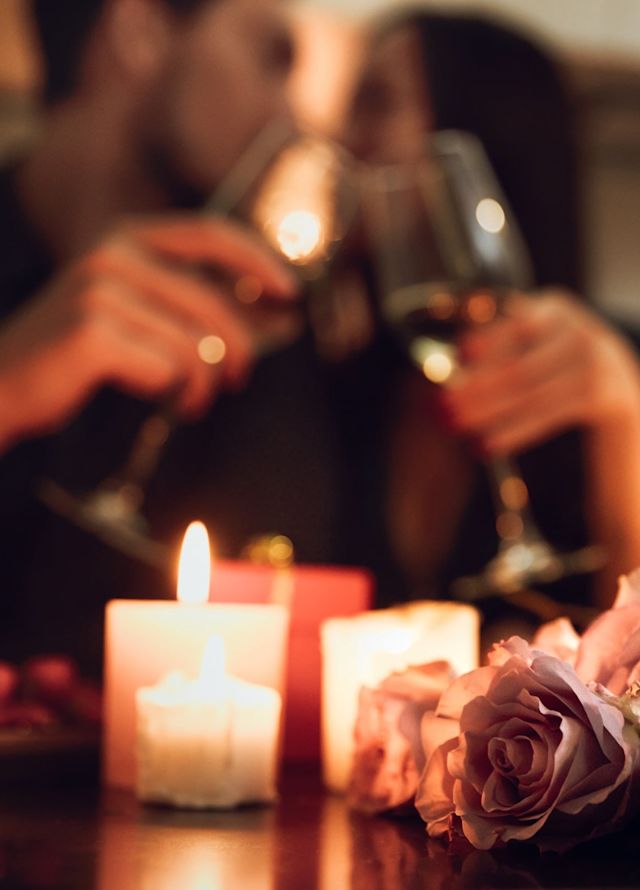 Closup of flowers and candles with couple drinking wine in the background